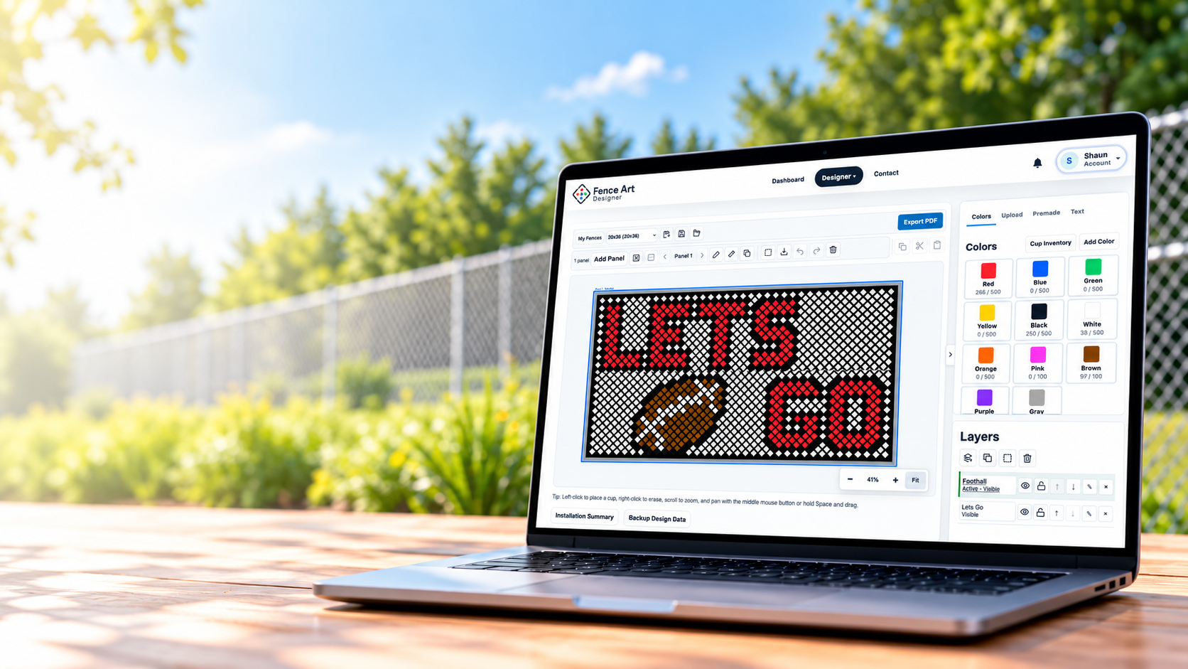 Laptop displaying Fence Art Designer with LETS GO football cup artwork beside an outdoor fence.